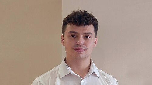 Rowan, a white man with brown hair wearing a white shirt, smiles at the camera