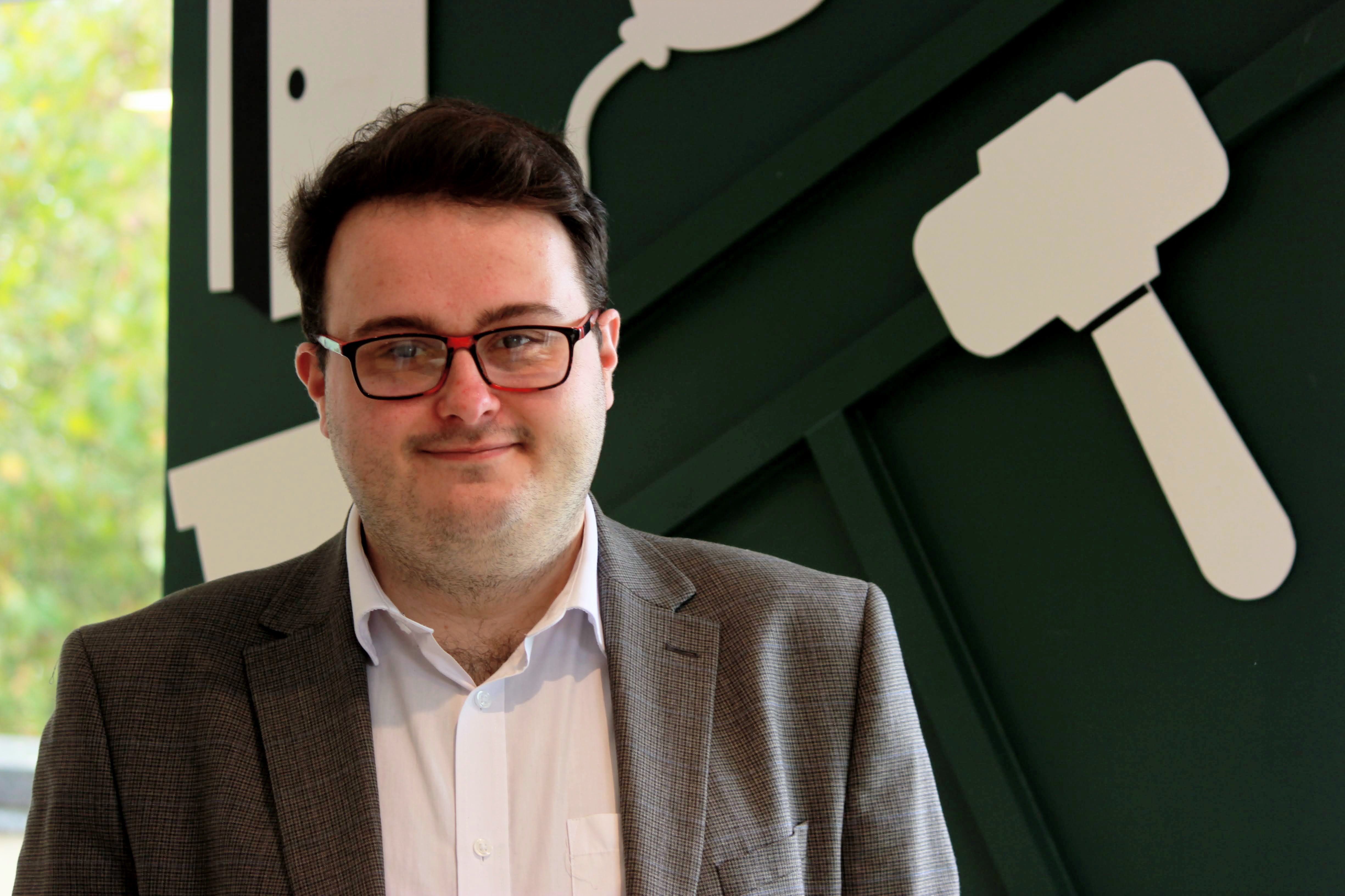 Harvey, a white man with brown hair and glasses, wearing a blazer and white collared shirt